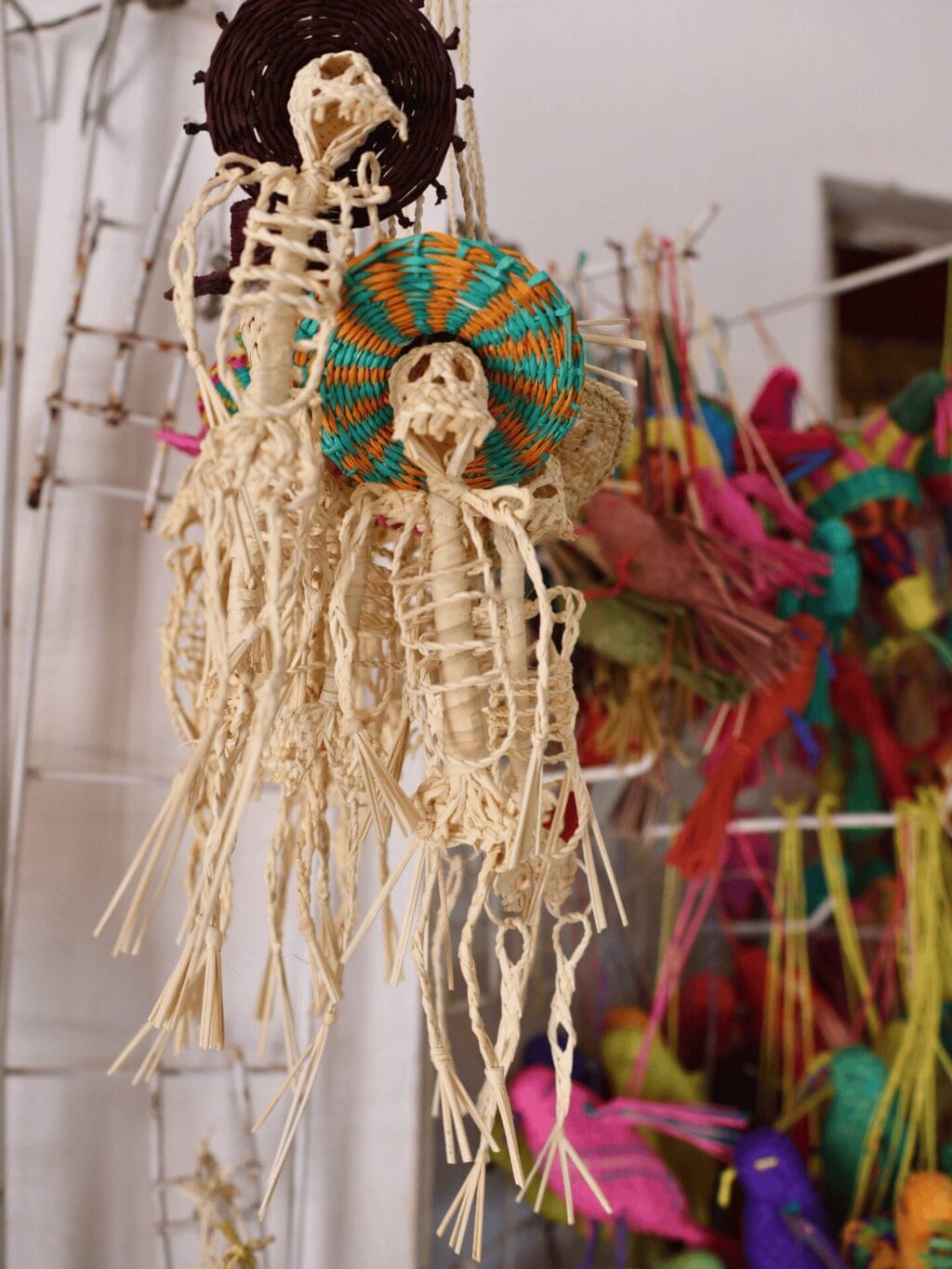 Miniskelette aus Stroh hängen hängen in einer Verkaufsauslage. Im Hintergrund sind andere farbige Artikel aus Stroh zu sehen